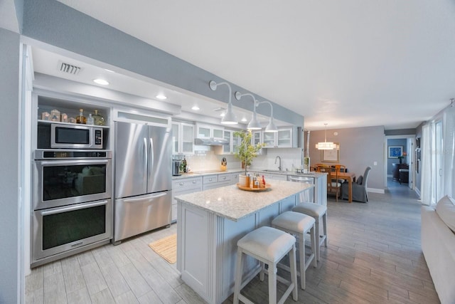 kitchen with a breakfast bar area, white cabinetry, stainless steel appliances, decorative light fixtures, and a center island