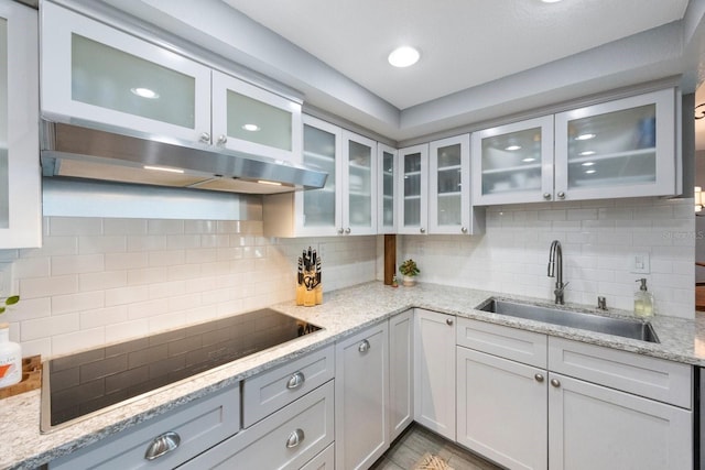 kitchen featuring black electric stovetop, tasteful backsplash, sink, and light stone counters