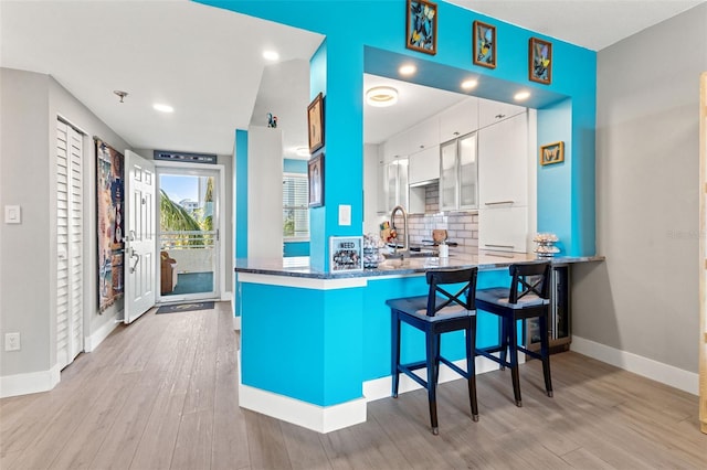 kitchen featuring decorative backsplash, kitchen peninsula, a breakfast bar, light hardwood / wood-style flooring, and white cabinets