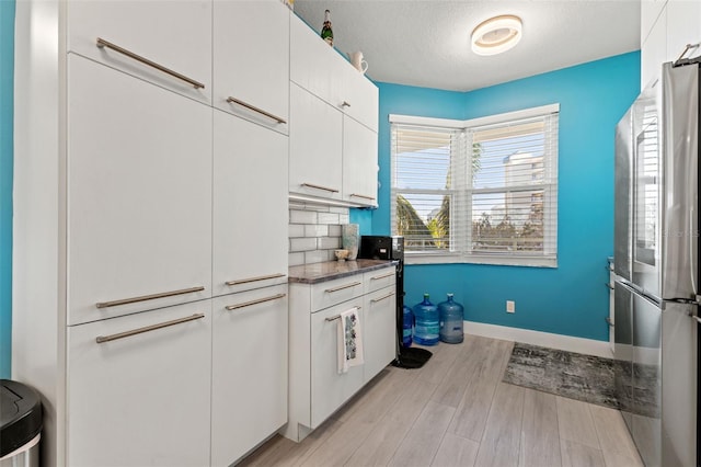 kitchen featuring white cabinetry, tasteful backsplash, stainless steel fridge, a textured ceiling, and light wood-type flooring