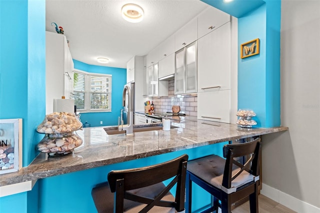 kitchen with kitchen peninsula, decorative backsplash, white cabinetry, and a breakfast bar