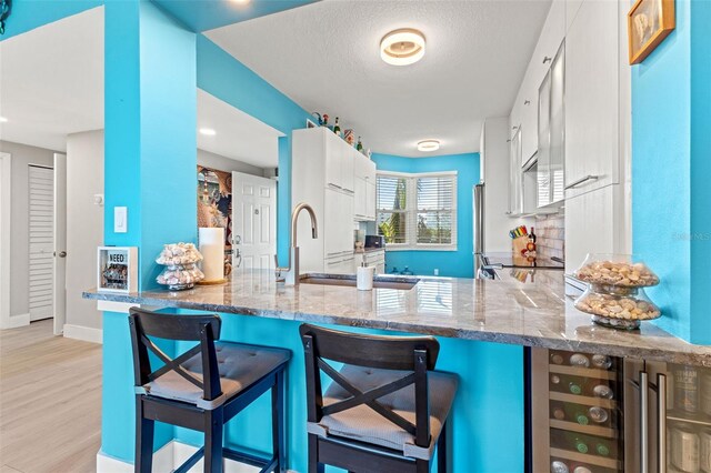 kitchen featuring stone counters, kitchen peninsula, light hardwood / wood-style flooring, and white cabinetry