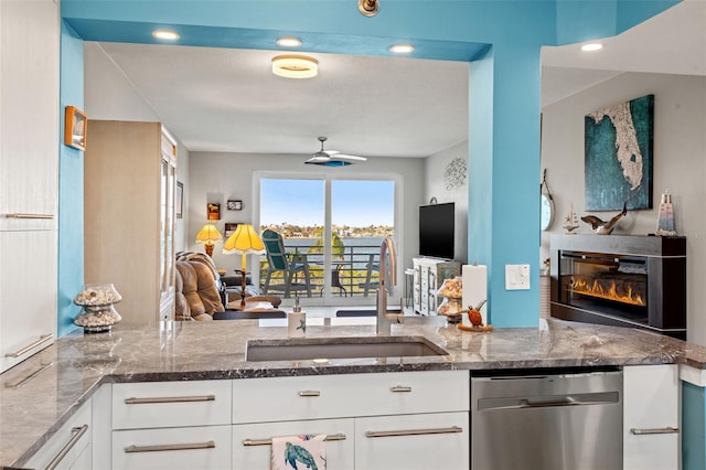 kitchen featuring white cabinetry, sink, ceiling fan, stainless steel dishwasher, and dark stone countertops