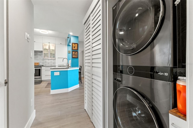 clothes washing area with light wood-type flooring, stacked washer / dryer, and sink