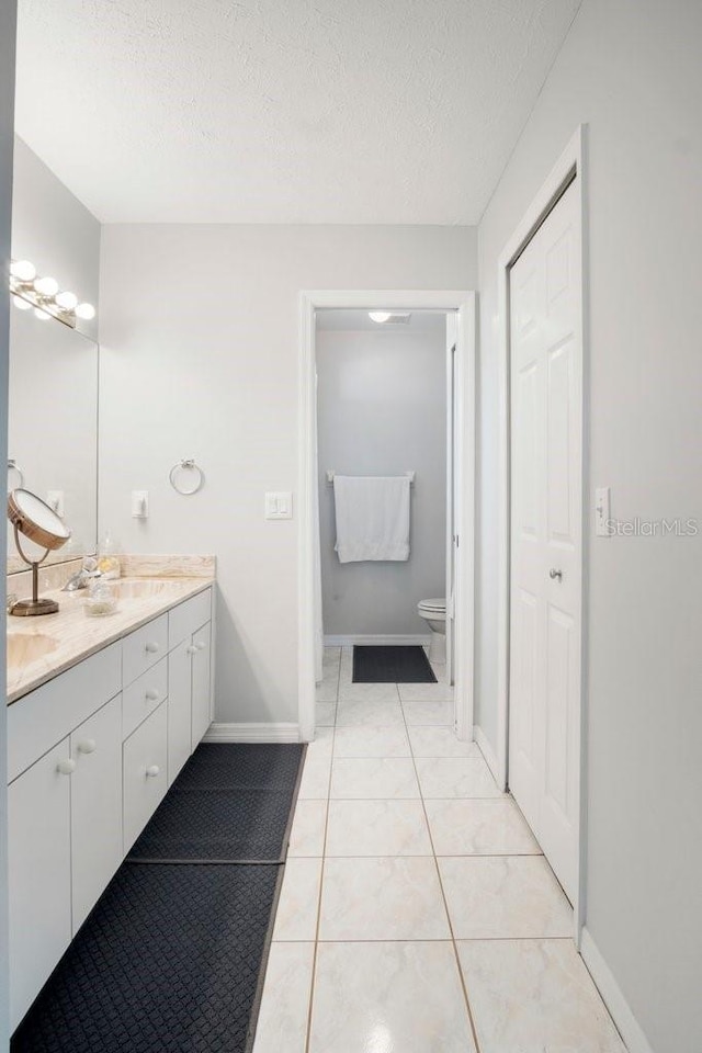 bathroom with tile patterned flooring, vanity, toilet, and a textured ceiling