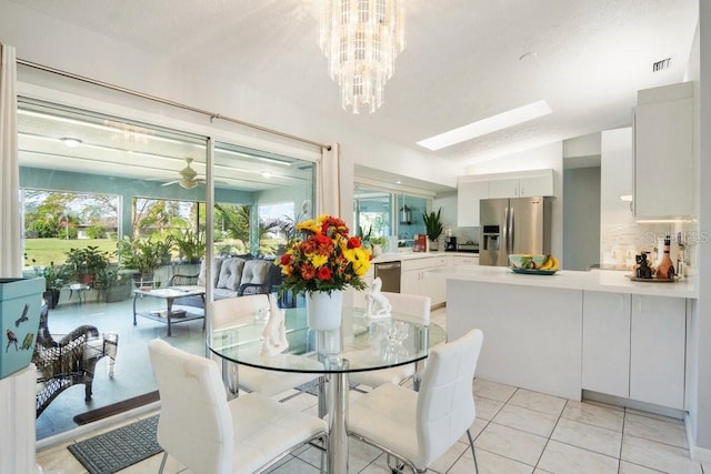 tiled dining room with ceiling fan with notable chandelier, a healthy amount of sunlight, and vaulted ceiling