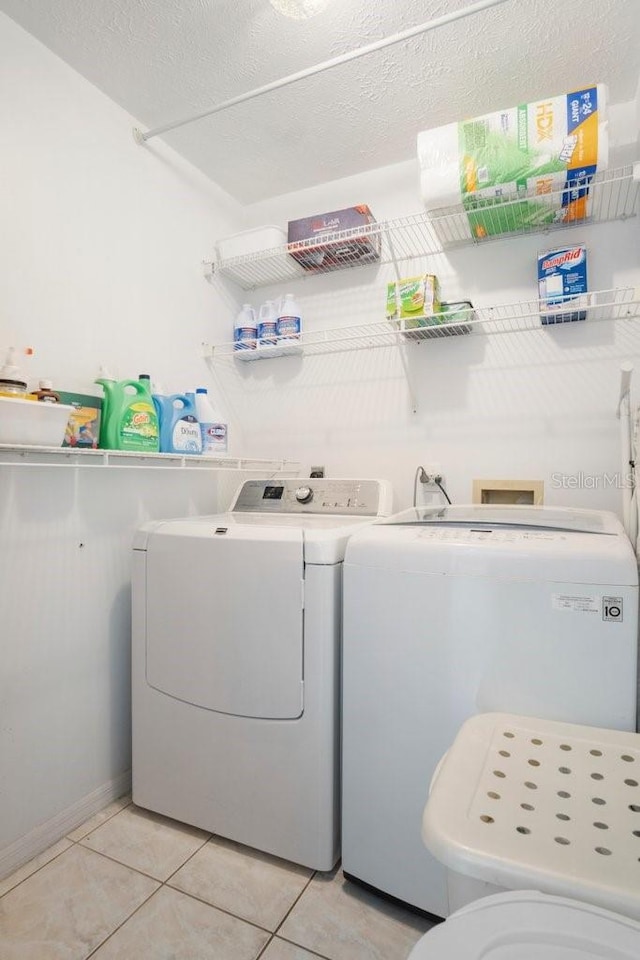 clothes washing area with washer and clothes dryer, light tile patterned floors, and a textured ceiling