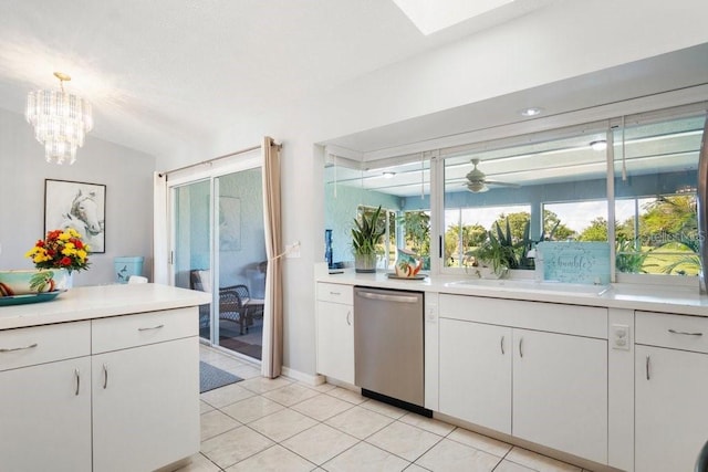 kitchen with stainless steel dishwasher, lofted ceiling with skylight, light tile patterned floors, white cabinetry, and hanging light fixtures