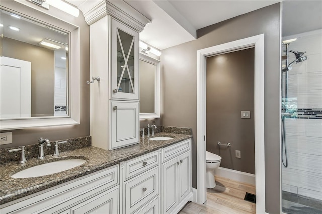 bathroom featuring hardwood / wood-style flooring, vanity, toilet, and a tile shower