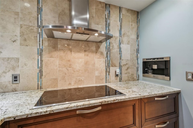 kitchen with black electric cooktop, wall chimney exhaust hood, and light stone counters