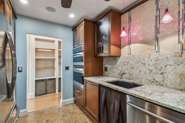 kitchen featuring stainless steel appliances, light stone counters, sink, ceiling fan, and pendant lighting