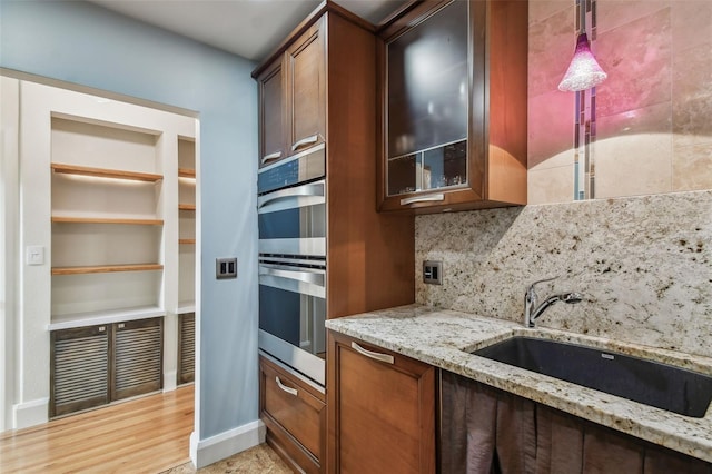 kitchen with stainless steel double oven, decorative light fixtures, light stone countertops, sink, and light hardwood / wood-style floors