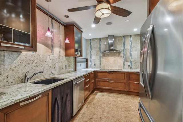 kitchen with light stone counters, wall chimney exhaust hood, hanging light fixtures, sink, and appliances with stainless steel finishes