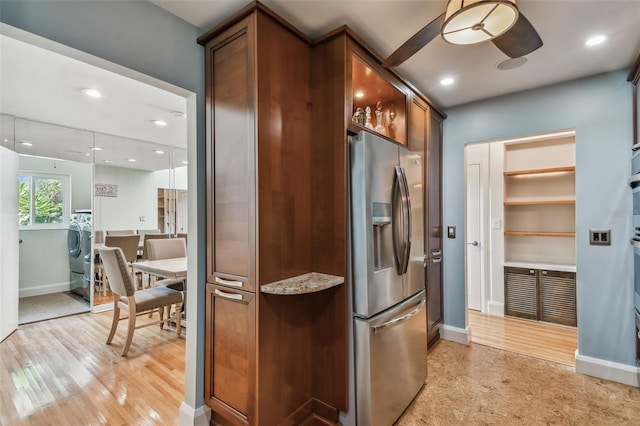 kitchen with stainless steel refrigerator with ice dispenser, hanging light fixtures, ceiling fan, light wood-type flooring, and washer / dryer