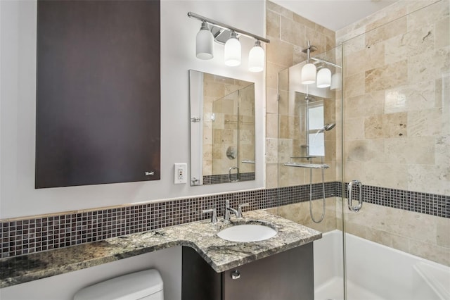 bathroom featuring toilet, vanity, decorative backsplash, and a shower with door