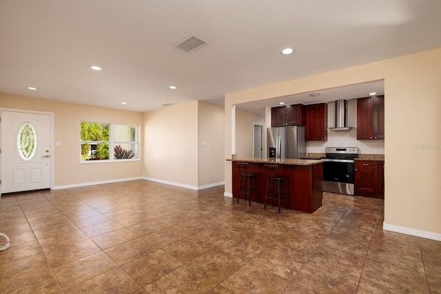 kitchen featuring wall chimney exhaust hood, appliances with stainless steel finishes, a kitchen island, and a kitchen breakfast bar