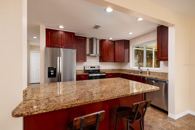 kitchen featuring wall chimney range hood, kitchen peninsula, sink, a breakfast bar, and appliances with stainless steel finishes