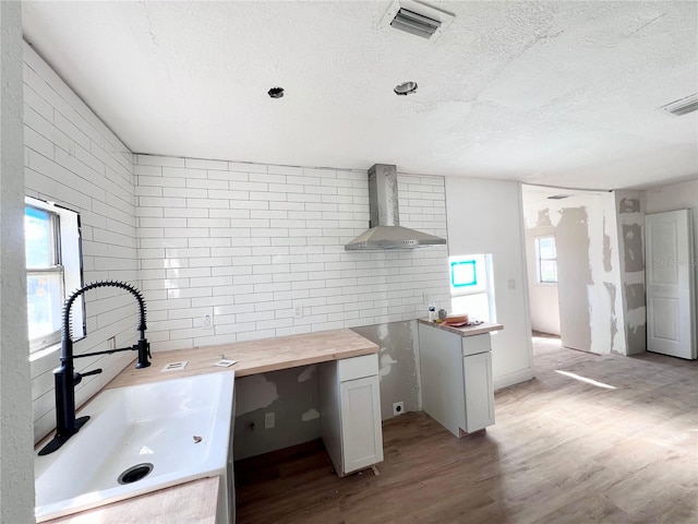 kitchen featuring wall chimney range hood, sink, butcher block countertops, white cabinetry, and light hardwood / wood-style floors