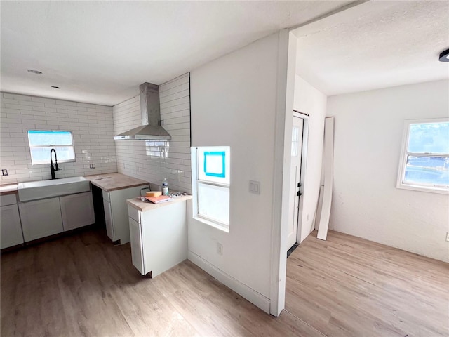 kitchen featuring wall chimney range hood, light hardwood / wood-style flooring, backsplash, wood counters, and sink