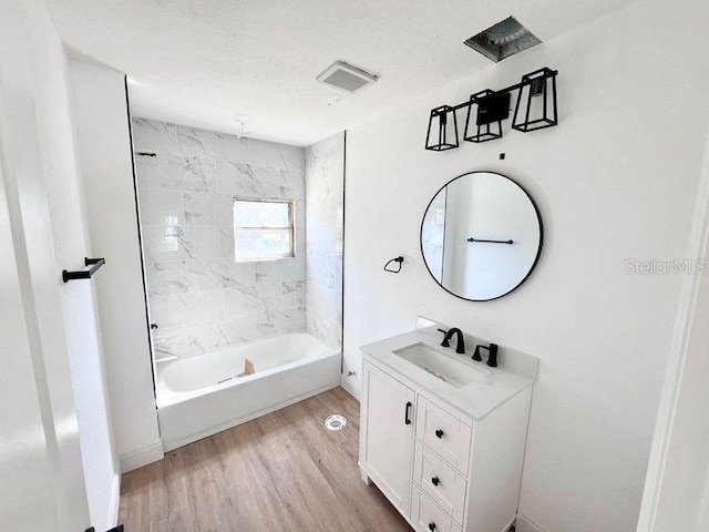 bathroom featuring vanity, hardwood / wood-style floors, tiled shower / bath combo, and a textured ceiling