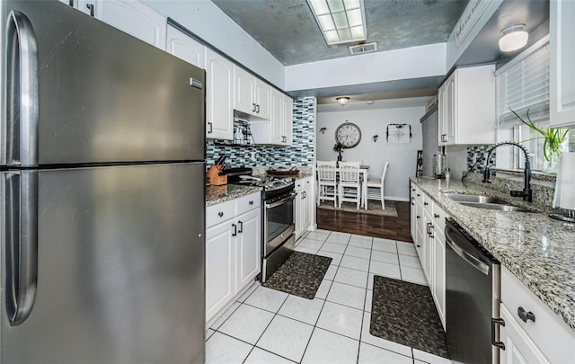 kitchen with appliances with stainless steel finishes, sink, stone countertops, white cabinetry, and light tile patterned floors