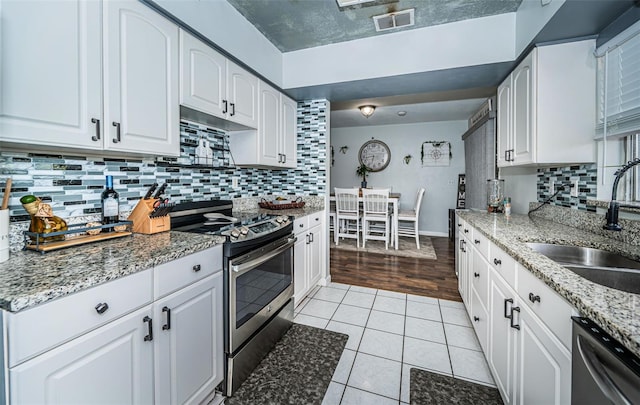 kitchen featuring sink, light stone countertops, light wood-type flooring, white cabinetry, and appliances with stainless steel finishes