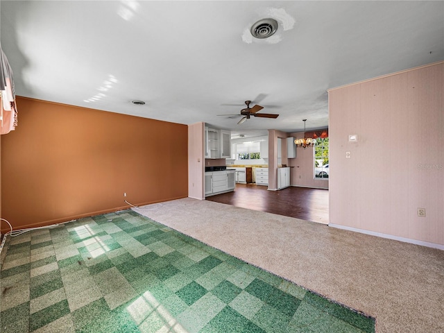 unfurnished living room featuring ceiling fan with notable chandelier and dark colored carpet