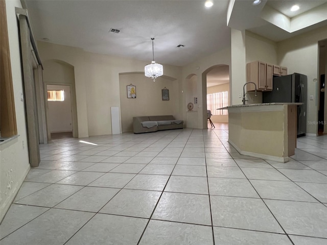 kitchen with kitchen peninsula, decorative light fixtures, light tile patterned floors, a chandelier, and black refrigerator