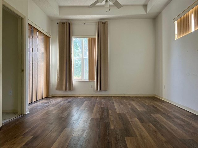 empty room featuring dark hardwood / wood-style floors, a tray ceiling, and ceiling fan