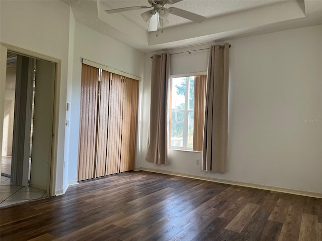 unfurnished room with a textured ceiling, ceiling fan, a tray ceiling, and dark hardwood / wood-style flooring