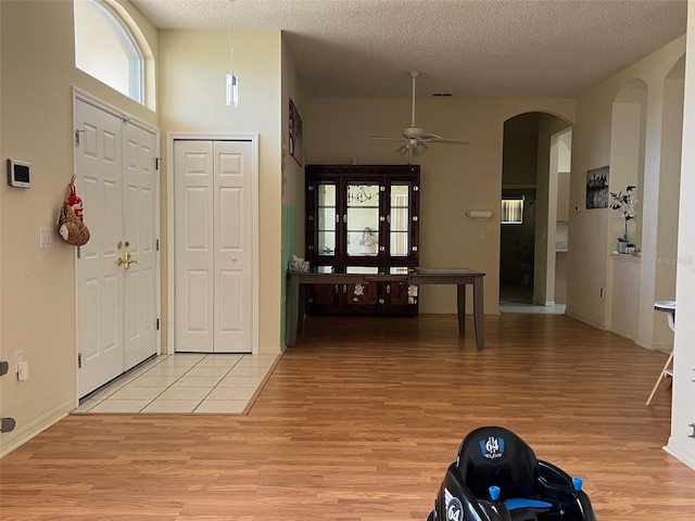 foyer with a towering ceiling, light hardwood / wood-style floors, a textured ceiling, and ceiling fan