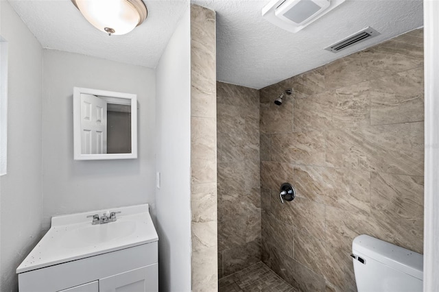 bathroom featuring vanity, a tile shower, a textured ceiling, and toilet