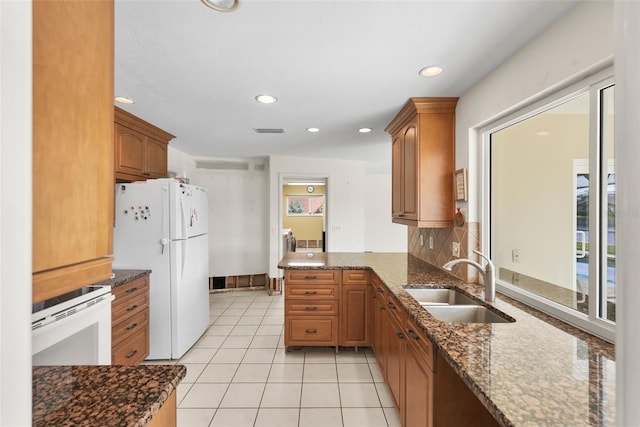 kitchen featuring white fridge, dark stone counters, sink, and kitchen peninsula