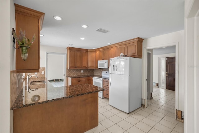 kitchen featuring white appliances, sink, backsplash, kitchen peninsula, and dark stone countertops