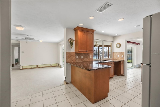 kitchen featuring kitchen peninsula, ceiling fan, white fridge, dark stone countertops, and light tile patterned floors