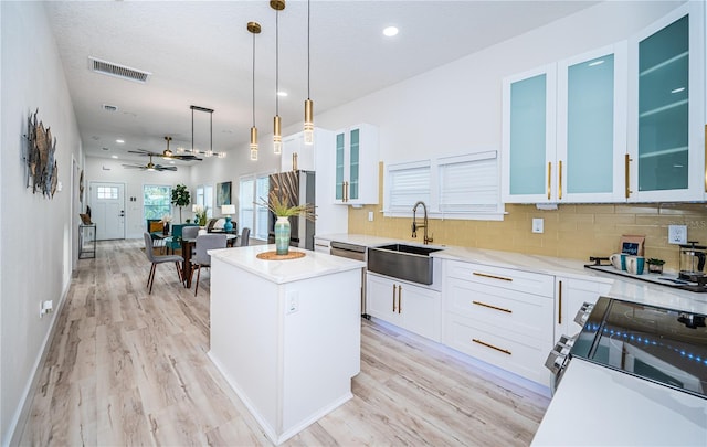 kitchen with sink, light wood-type flooring, a center island, ceiling fan, and decorative light fixtures