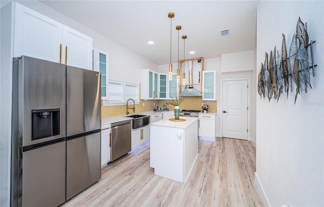 kitchen featuring a center island, white cabinetry, stainless steel appliances, decorative light fixtures, and light hardwood / wood-style flooring