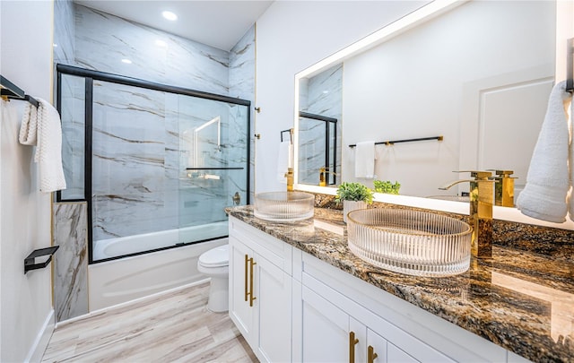 full bathroom with toilet, enclosed tub / shower combo, vanity, and wood-type flooring