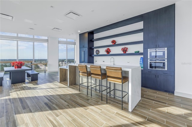 777 3rd Ave N Unit 1203, Saint Petersburg, FL 33701 - kitchen with light wood-type flooring, expansive windows, open shelves, a kitchen bar, and stainless steel double oven