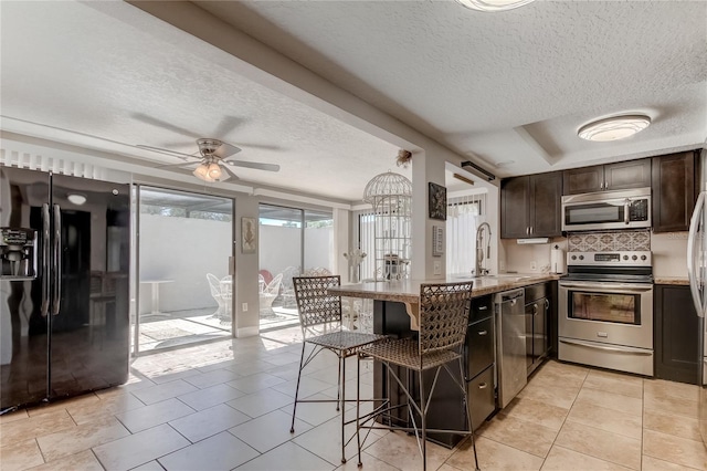 kitchen featuring a kitchen bar, kitchen peninsula, stainless steel appliances, ceiling fan, and sink