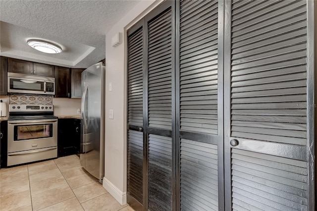 kitchen with appliances with stainless steel finishes, tasteful backsplash, a textured ceiling, dark brown cabinetry, and light tile patterned floors