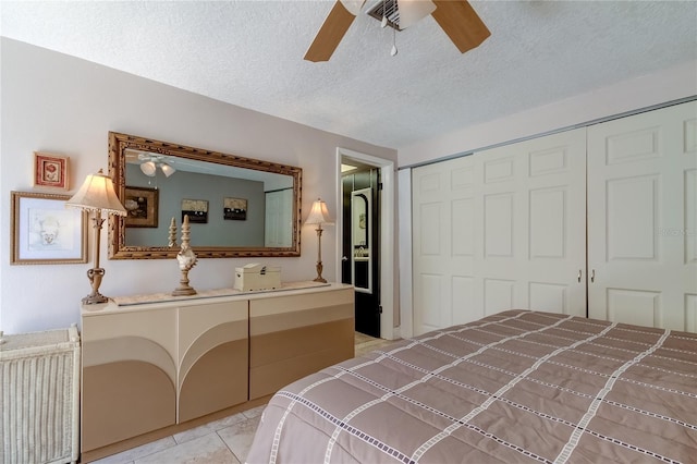 bedroom with ceiling fan, light tile patterned floors, a textured ceiling, and a closet