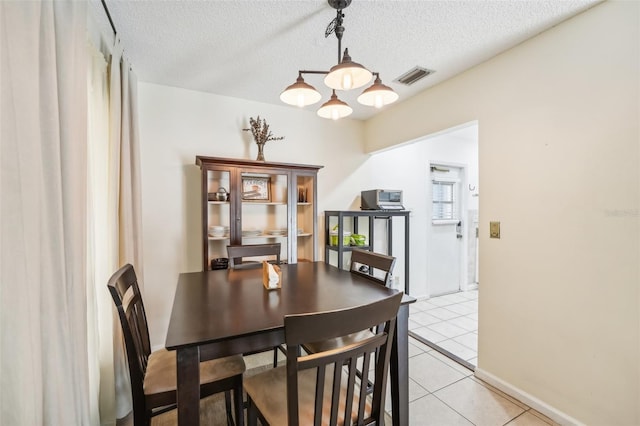 dining space with a chandelier, a textured ceiling, and light tile patterned flooring