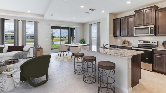 kitchen featuring appliances with stainless steel finishes, sink, backsplash, light stone counters, and a kitchen island with sink