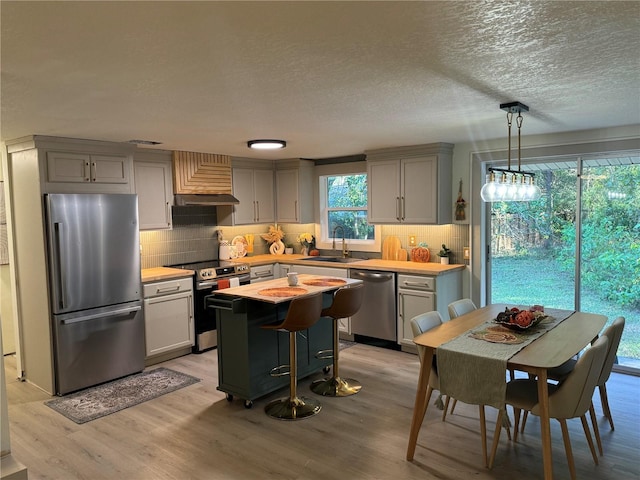 kitchen with stainless steel appliances, sink, a center island, decorative light fixtures, and light wood-type flooring