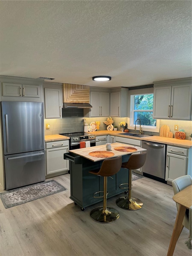 kitchen featuring custom range hood, sink, light wood-type flooring, appliances with stainless steel finishes, and a textured ceiling