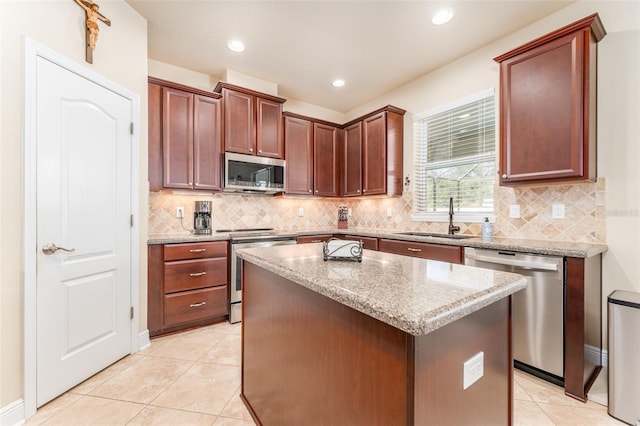 kitchen with light stone counters, stainless steel appliances, light tile patterned floors, sink, and a center island