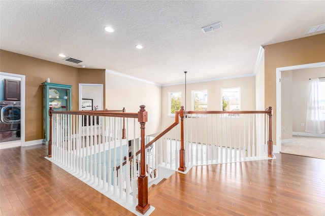 hall featuring hardwood / wood-style flooring, a textured ceiling, washer / clothes dryer, and crown molding