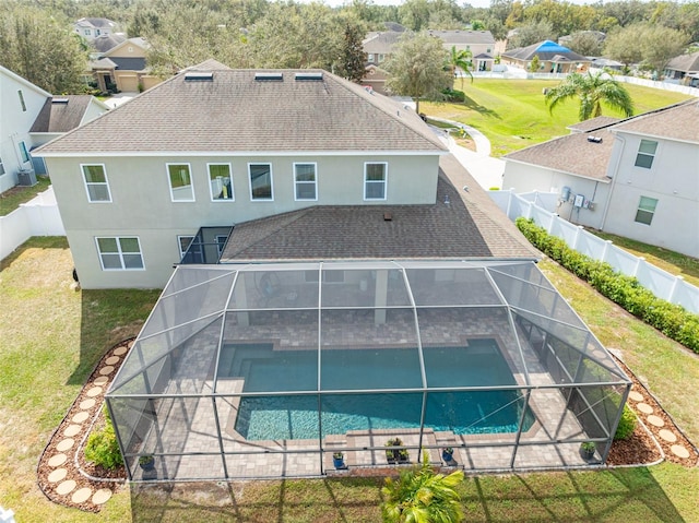 rear view of property featuring glass enclosure, a lawn, a fenced in pool, and a patio area