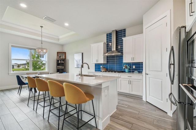 kitchen featuring an island with sink, white cabinetry, wall chimney exhaust hood, and sink